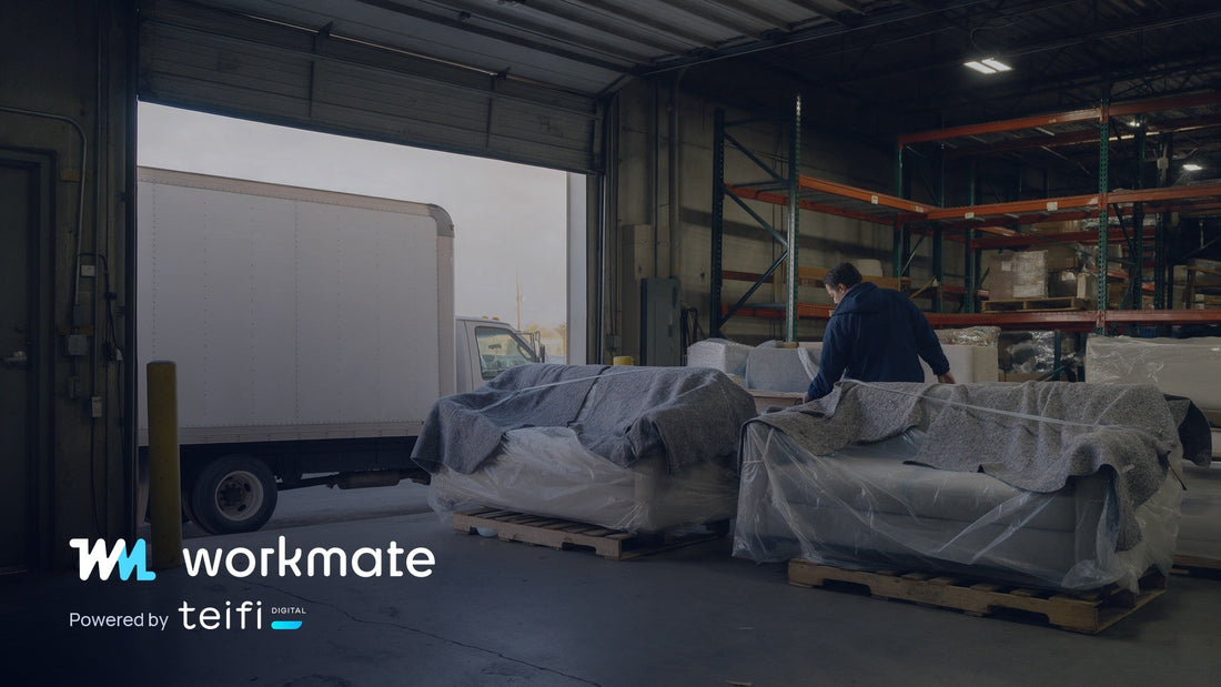 Two made-to-order sofas wrapped in moving blankets on pallets at a furniture warehouse dock, with a delivery truck backed up to the open door.